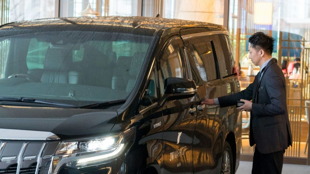A man in a suit standing next to a black car